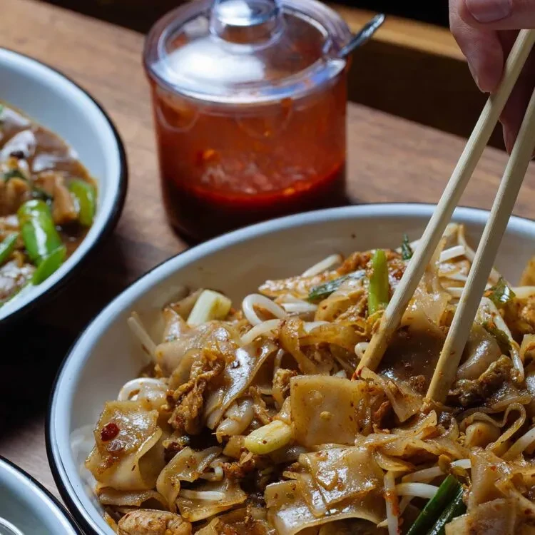Close-up: Chopsticks poised above stir-fried flat rice noodles.