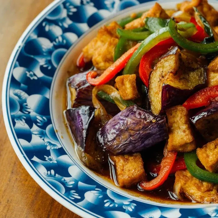 Stir-fried eggplant, peppers, and tofu in a blue and white patterned bowl.