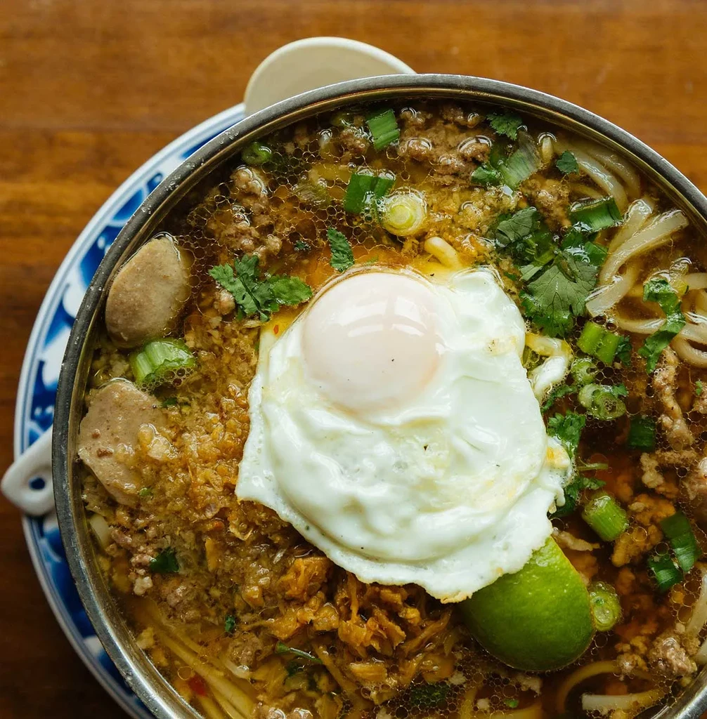 Overhead view of noodle soup with egg, ground meat, and lime.