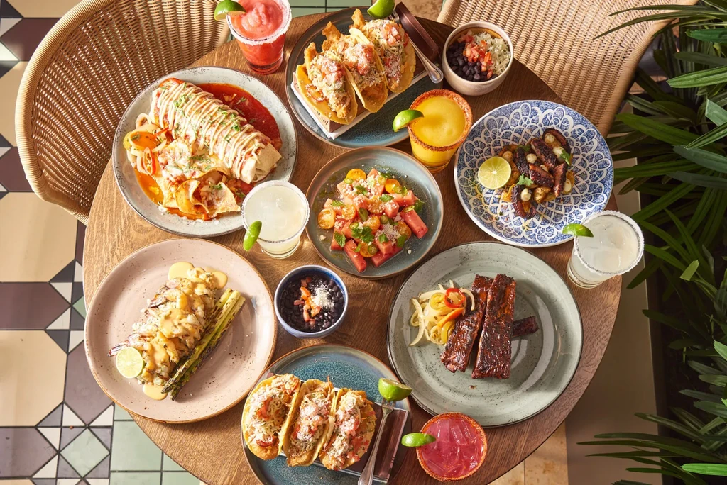 Overhead shot of a wooden table with Mexican food and colorful margaritas.