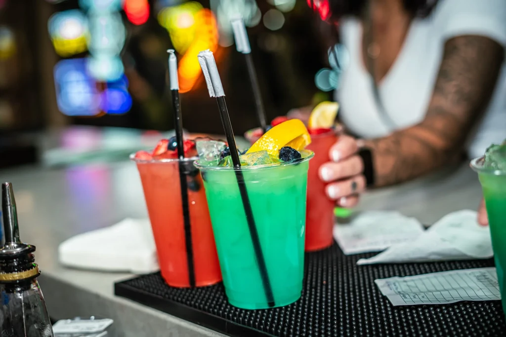 Teal and red fruit drinks on a bar mat with blurred background.