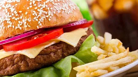 Cheeseburger, golden french fries, and a dark beverage on a white plate.