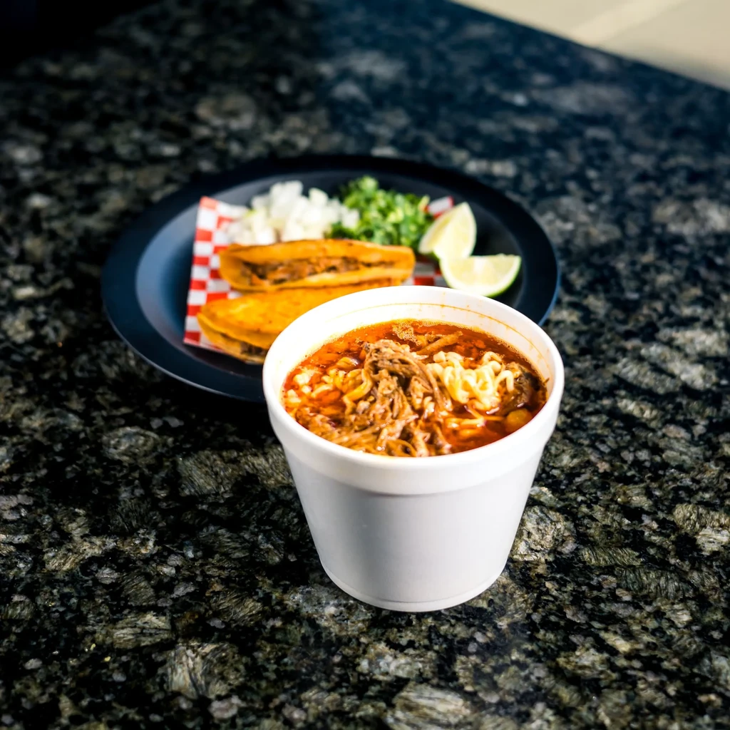 Birria ramen and two birria tacos with onions, cilantro, and lime.
