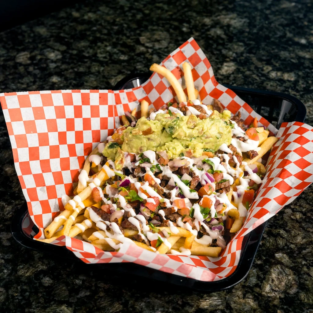 Loaded carne asada fries with guacamole and pico de gallo in a basket.
