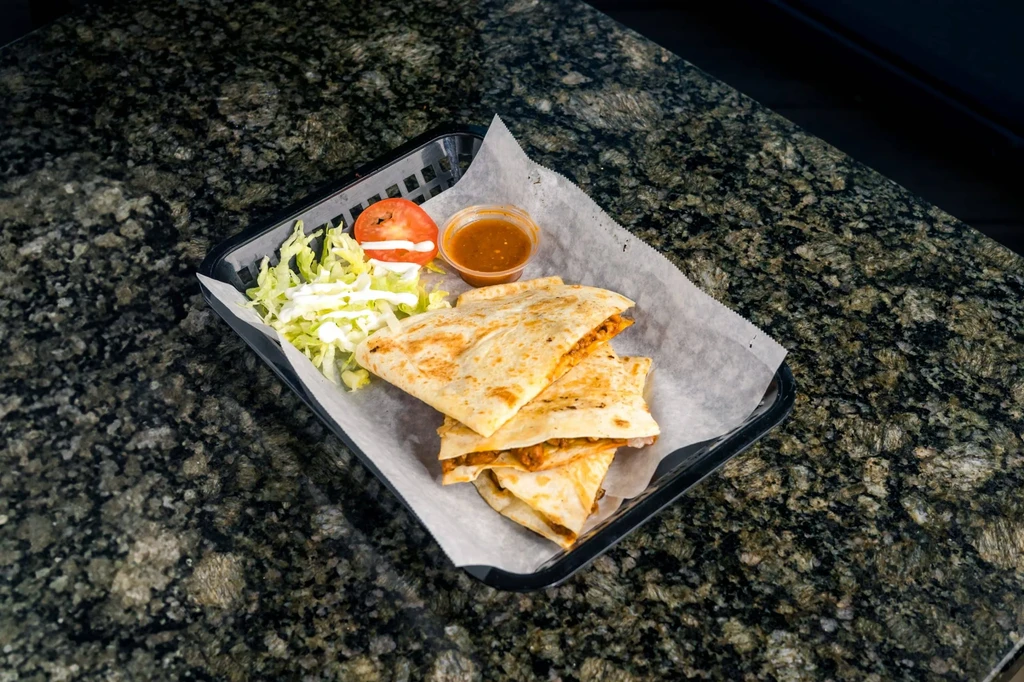 Three quesadilla wedges with lettuce, tomato, white sauce, and salsa.