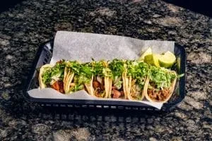 Five street tacos with meat, lettuce, and lime.