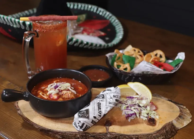 Vibrant Mexican stew, michelada, taco, and snacks on wood.