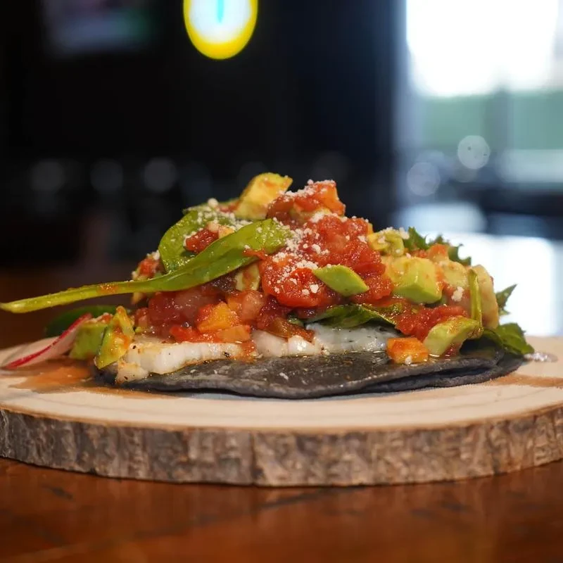 Charcoal tostada with creamy sauce, red salsa, avocado, and greens.