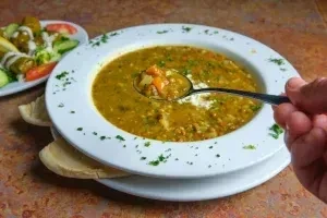 Hand scooping thick greenish-brown vegetable soup.
