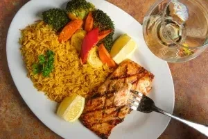 Grilled salmon, yellow rice, colorful vegetables, and lemon on a plate.