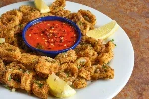 Golden-brown fried calamari, red dipping sauce, and lemon wedges.