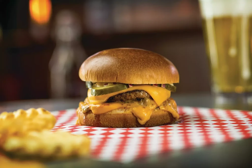 Close-up cheeseburger with melted cheese, pickles, onions, fries, and beer.