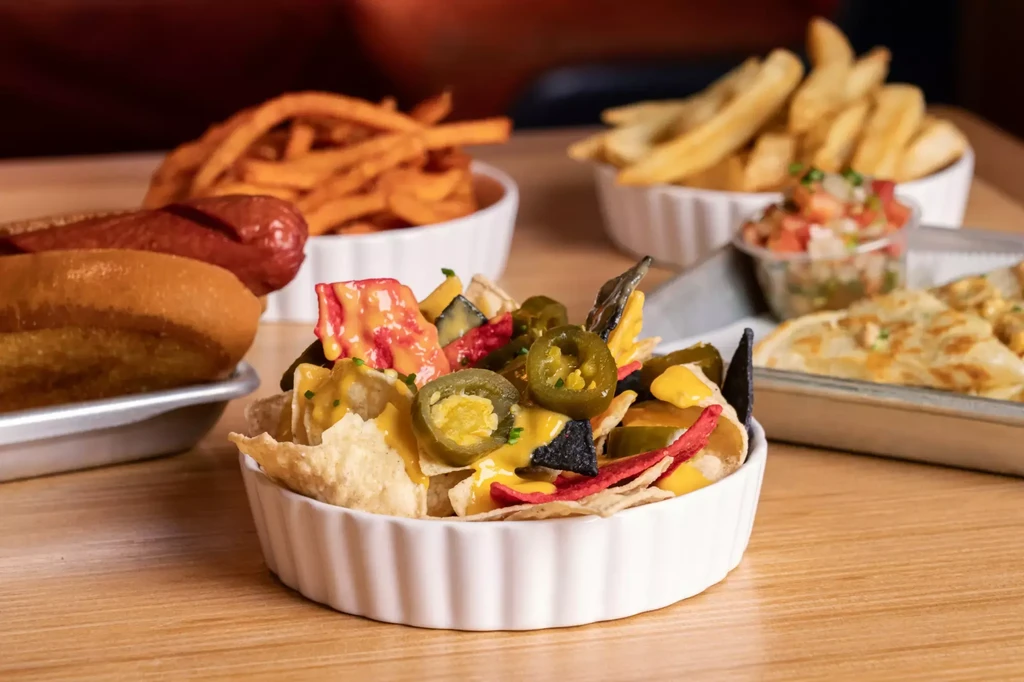 Close-up of cheesy nachos with jalapeños, fries, and a hot dog.