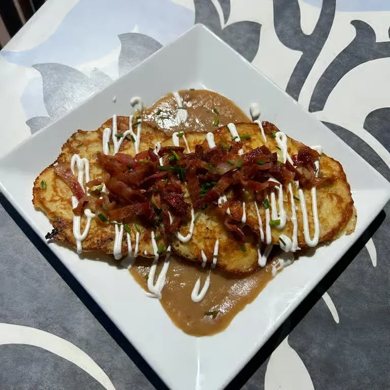 Golden fritters with bacon, chives, white and brown sauces on a plate.