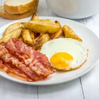 Close-up of a breakfast plate: egg, bacon, potato wedges, and toast.