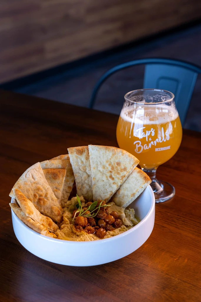 Bowl of hummus and pita with a "Taps & Barrels" amber beer.