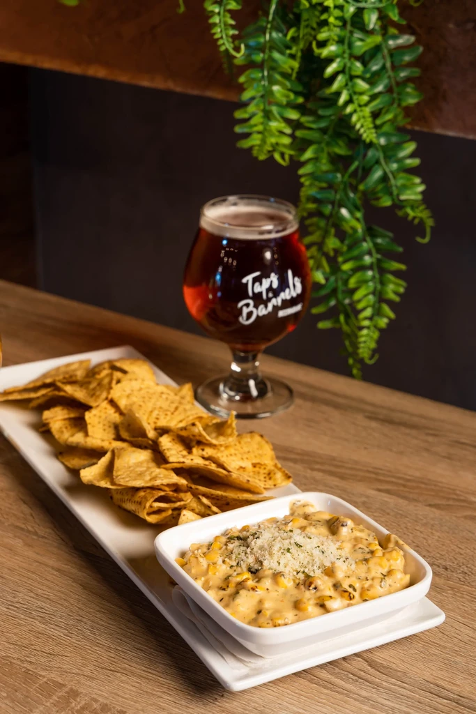 Golden-brown tortilla chips, corn dip, and beer on wood.