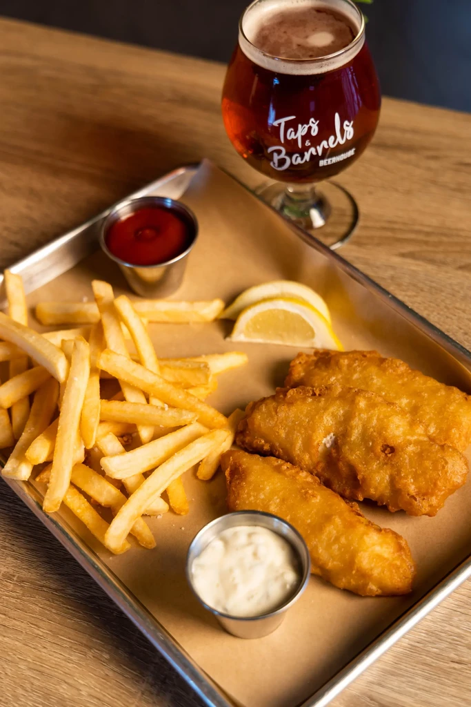 Fish and chips, sauces, lemon, and a Taps & Barrels beer.