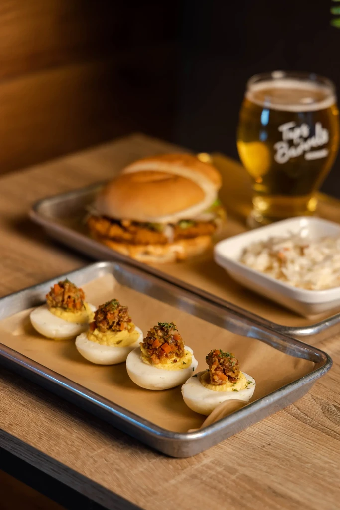 Four deviled eggs, burger, beer, and coleslaw on a wooden table.
