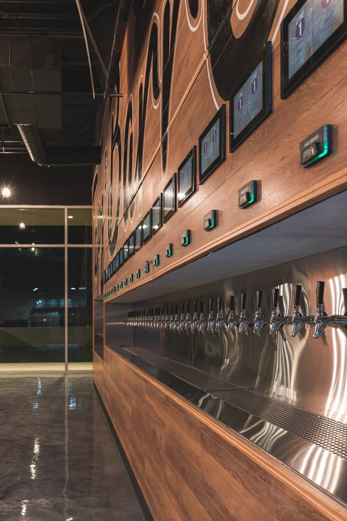 Sleek self-pour beer tap wall with digital screens and wooden panels.