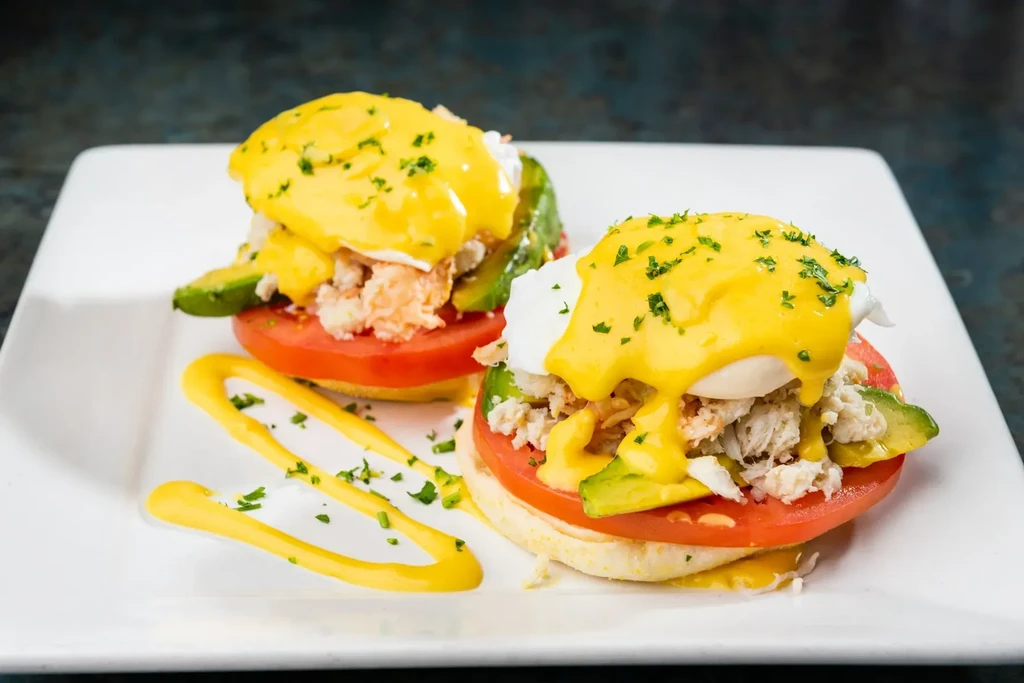 Two crab, avocado, tomato Eggs Benedict with hollandaise sauce.