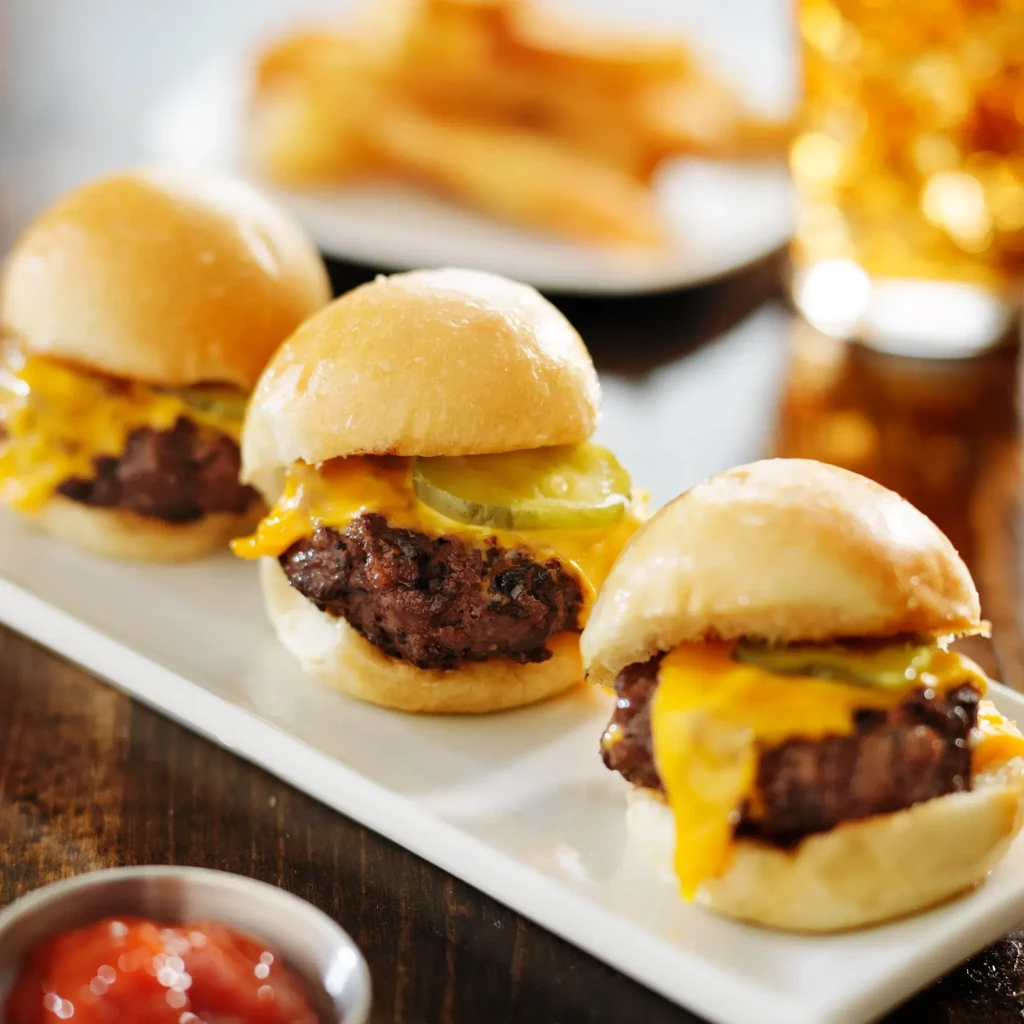 Three cheeseburger sliders with melted cheese, pickles, fries, and drink.