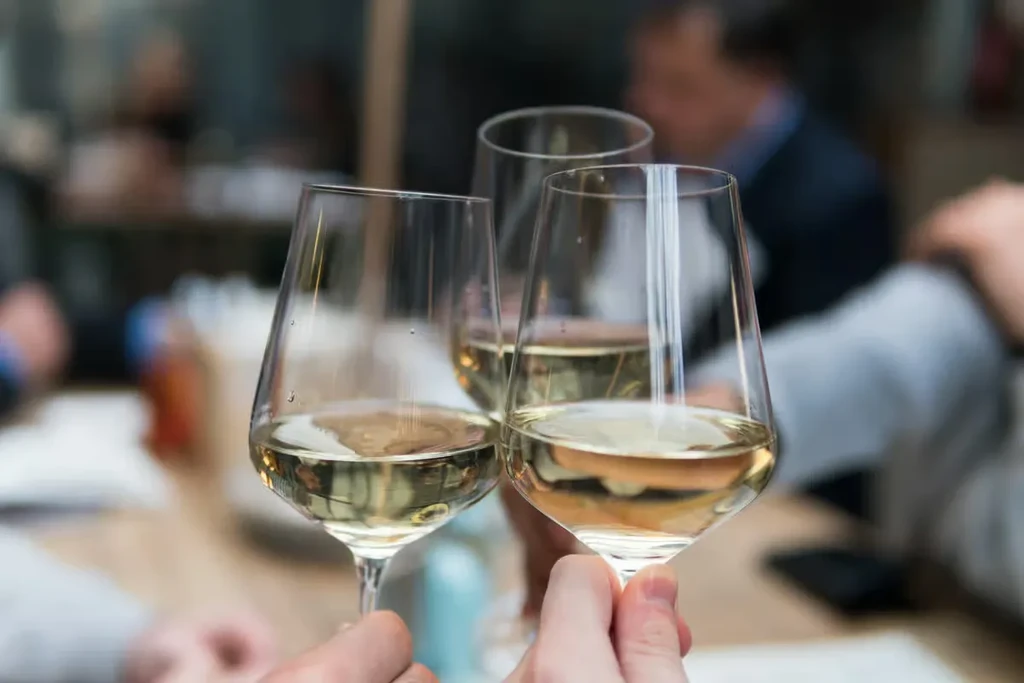 Three white wine glasses clinking in a toast with blurry background.