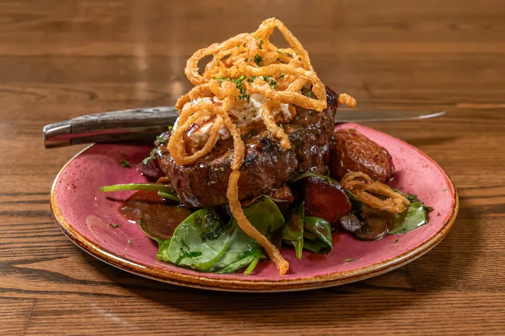 Seared steak with fried onions, creamy sauce, spinach, and vegetables.