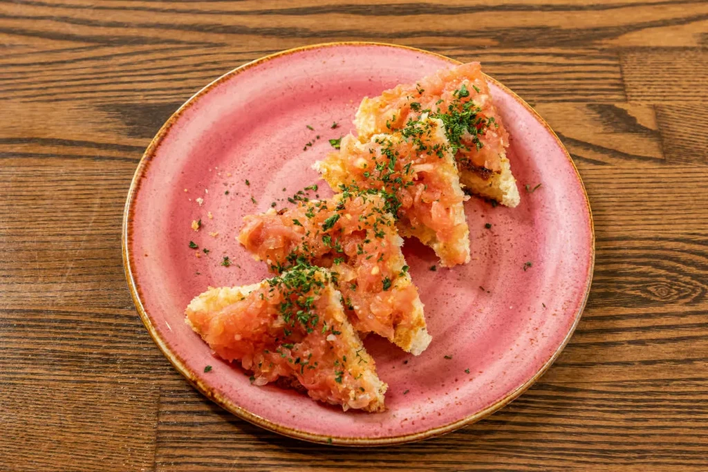 Four triangular bruschetta pieces topped with tomato and green herbs.