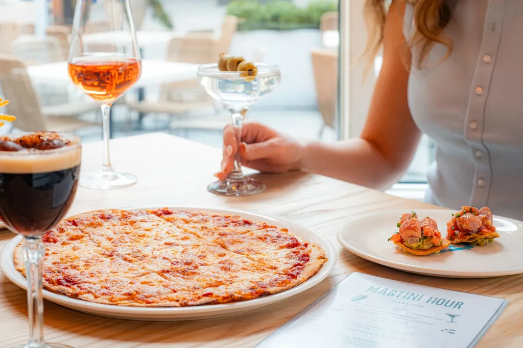 Restaurant table with cheese pizza, martini, appetizers, and a 'Martini Hour' menu.