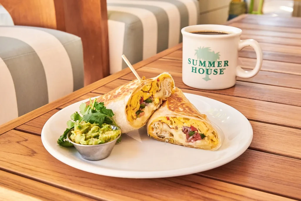 Cut breakfast burrito with eggs, guacamole, and coffee on a wooden table.
