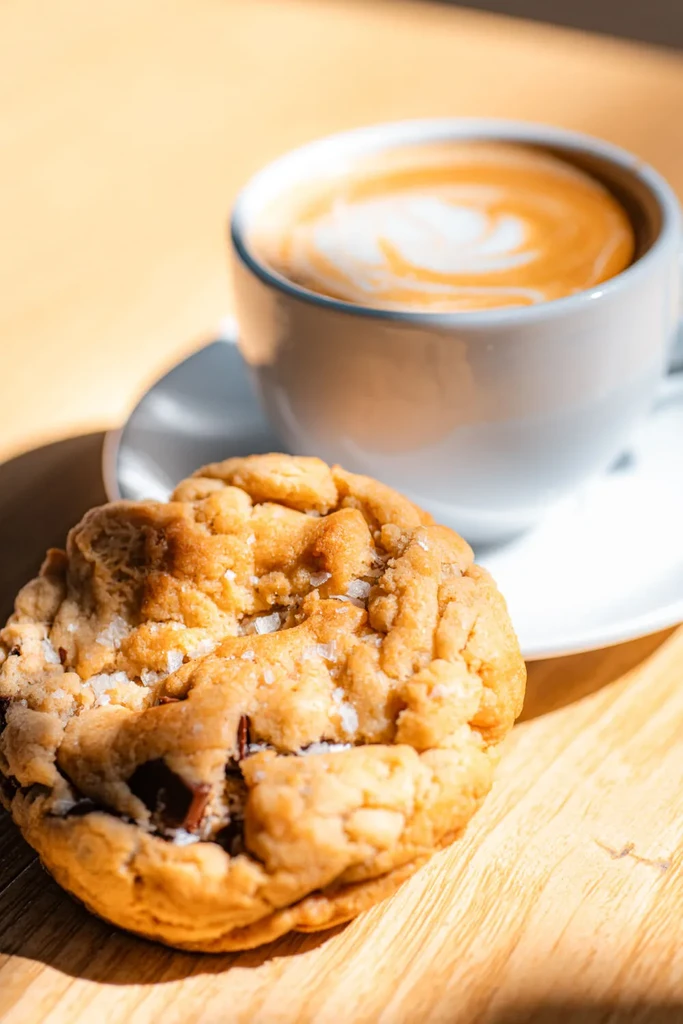 Close-up of sea salt chocolate chip cookie and latte on wood.
