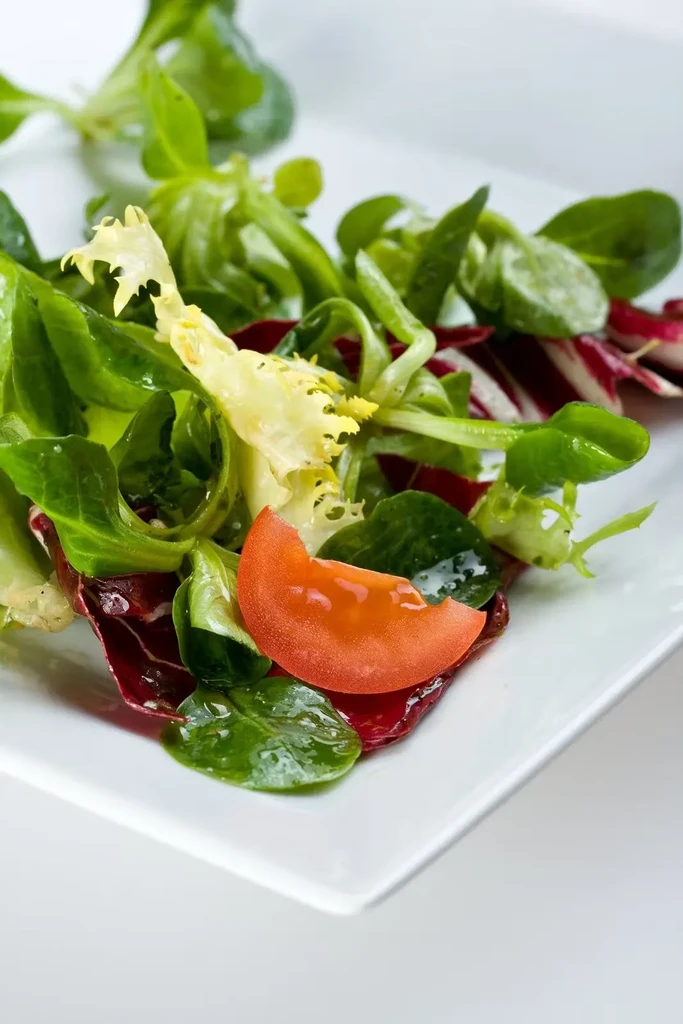 Fresh mixed green salad with a bright tomato on a white plate.