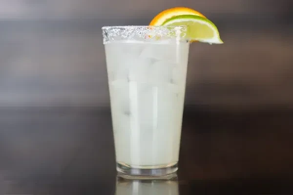 Glass with cloudy drink, ice, salted rim, orange, and lime.