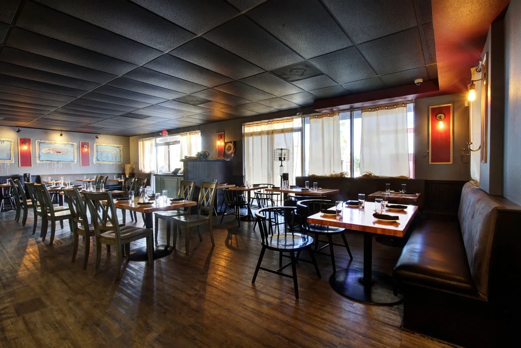 Empty restaurant dining room with warm lighting, dark wood, and marine art.