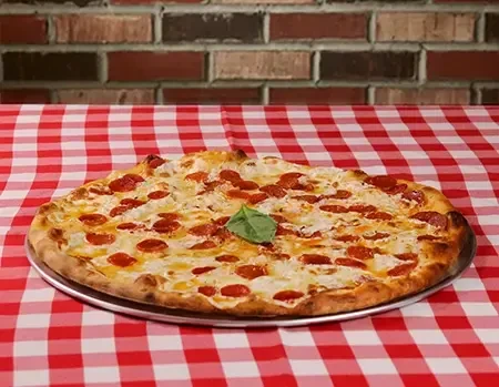 Round pepperoni pizza with cheese, basil leaf, on checkered table.