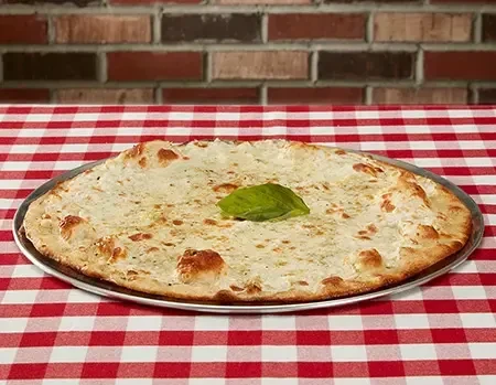 Round white pizza with cheese and basil on a checkered tablecloth.
