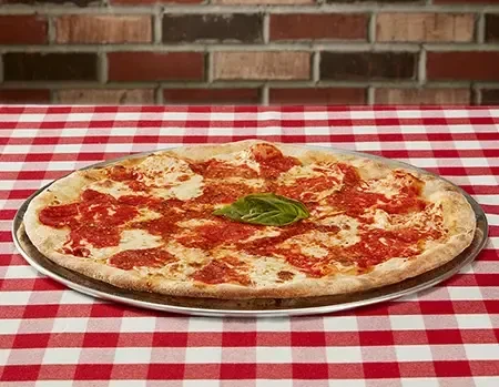 Margherita pizza on a checkered tablecloth, brick wall background.