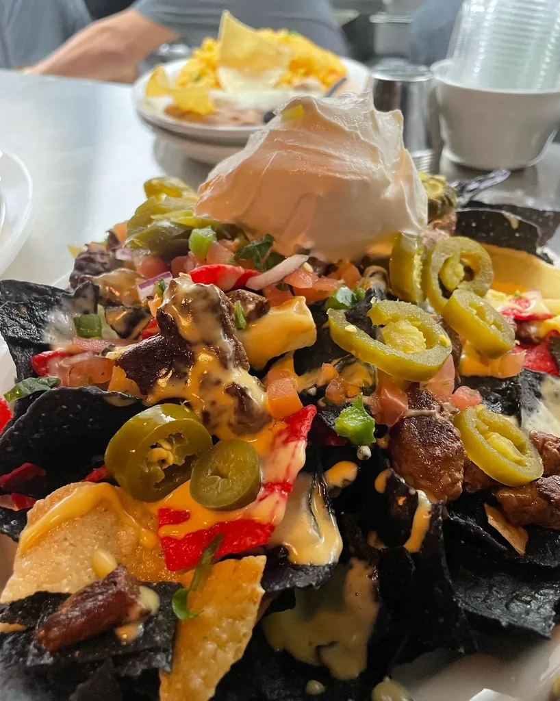 Large plate of black tortilla nachos with cheese, sour cream, and toppings.