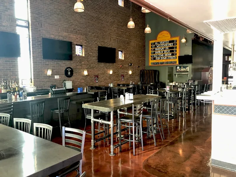 Empty brewpub interior with long bar, brick walls, and varied seating.