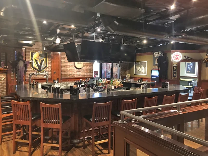 Dimly lit sports bar interior with Golden Knights logo, bar, and TVs.