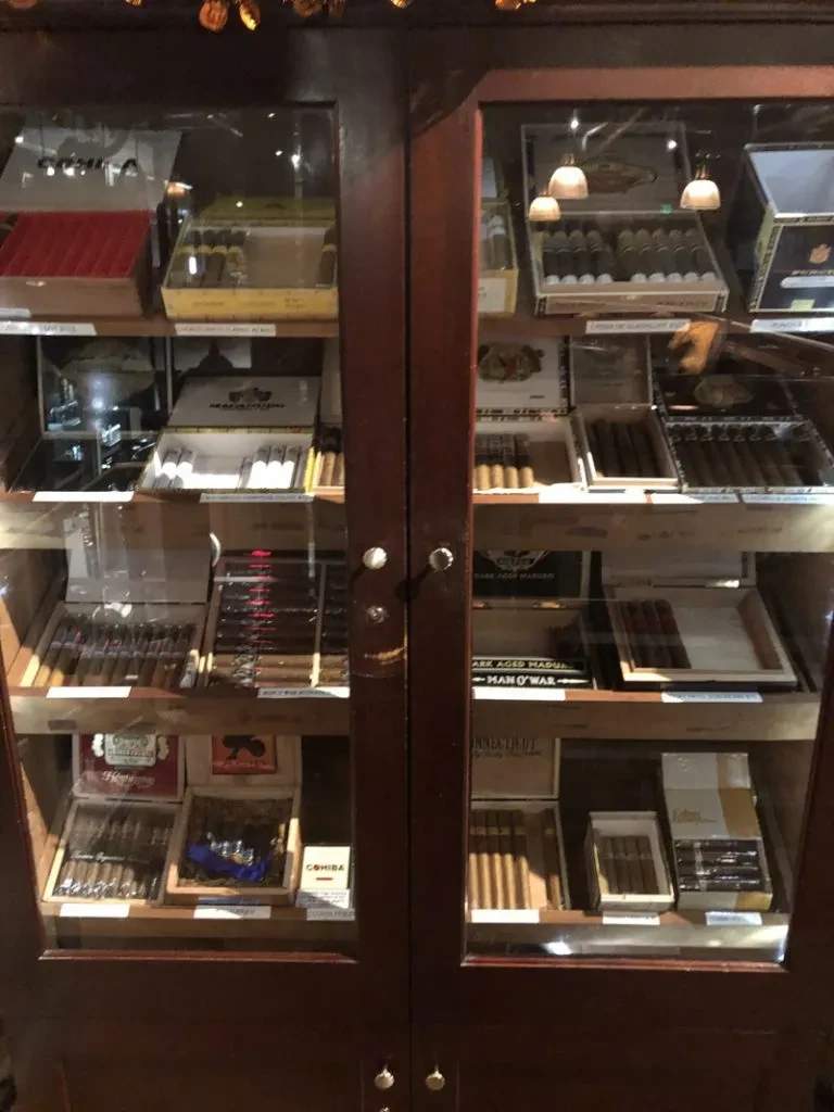Dark wooden humidor with glass doors, full of cigar boxes.