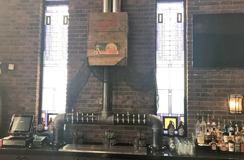 Industrial pipe beer tap system on brick wall, with ALE BEER sign.