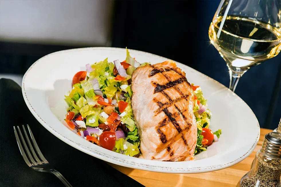 Grilled salmon, colorful salad, white wine, and table setting.
