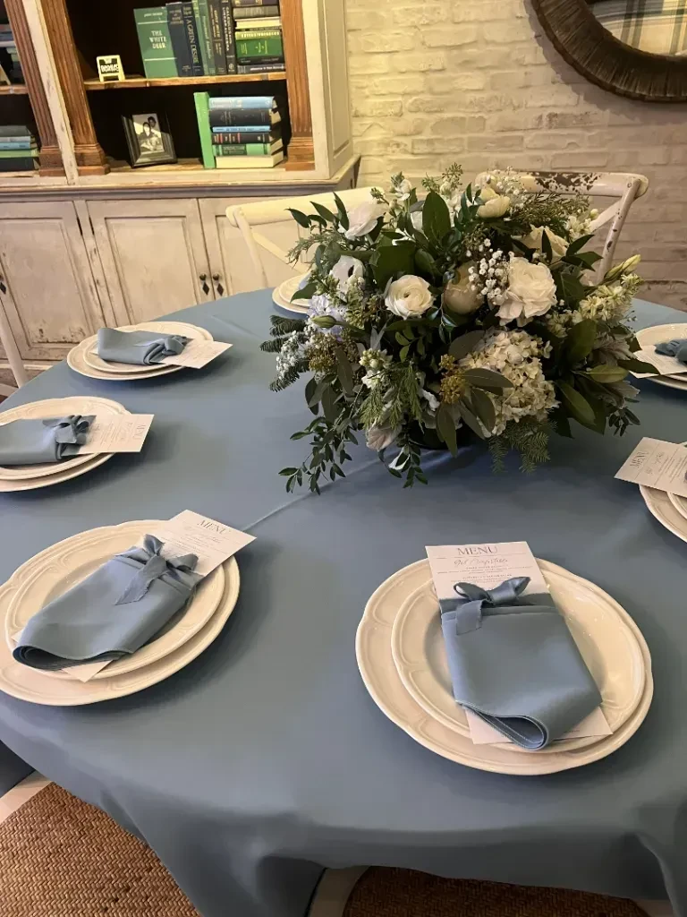 Blue-draped table with white place settings and white floral centerpiece.