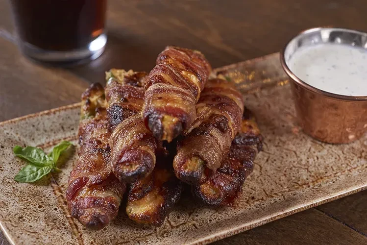 Plate of crispy bacon-wrapped items, basil, and herb dipping sauce.