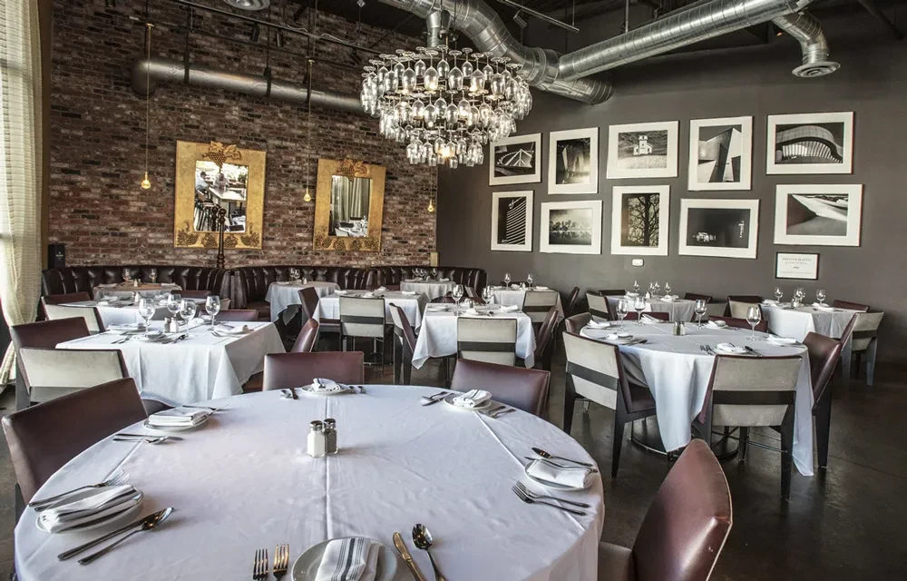 Empty industrial-chic restaurant: brick, leather seating, wine glass chandelier.
