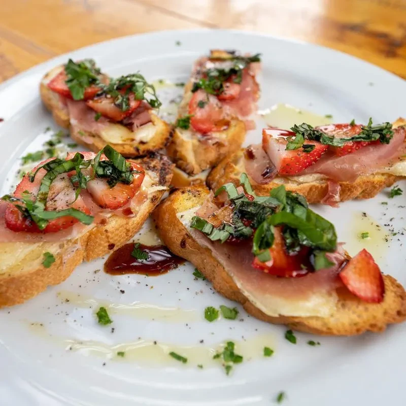 Bruschetta topped with prosciutto, cheese, strawberries, and fresh basil.