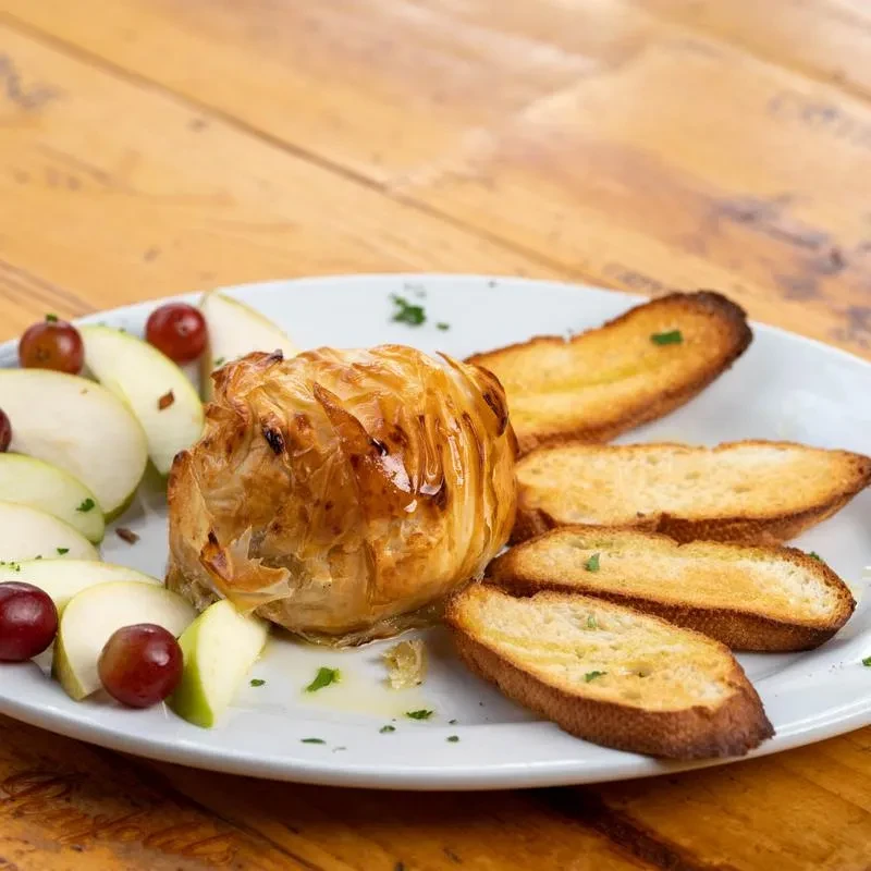 Baked brie pastry, apples, grapes, and toast on a rustic table.