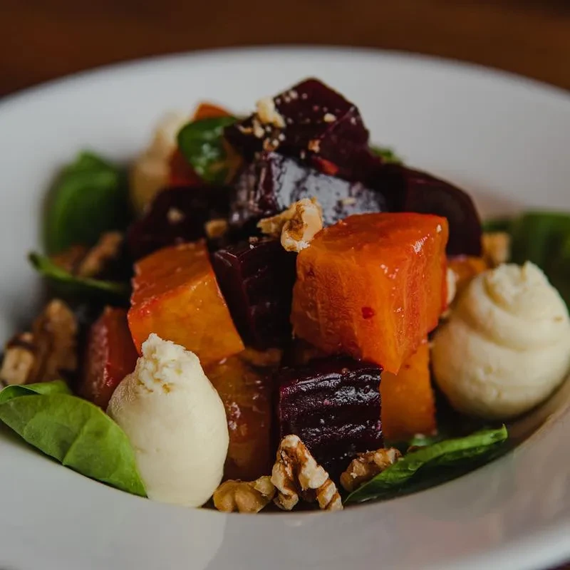 Roasted beets, walnuts, creamy cheese, and greens in white bowl.